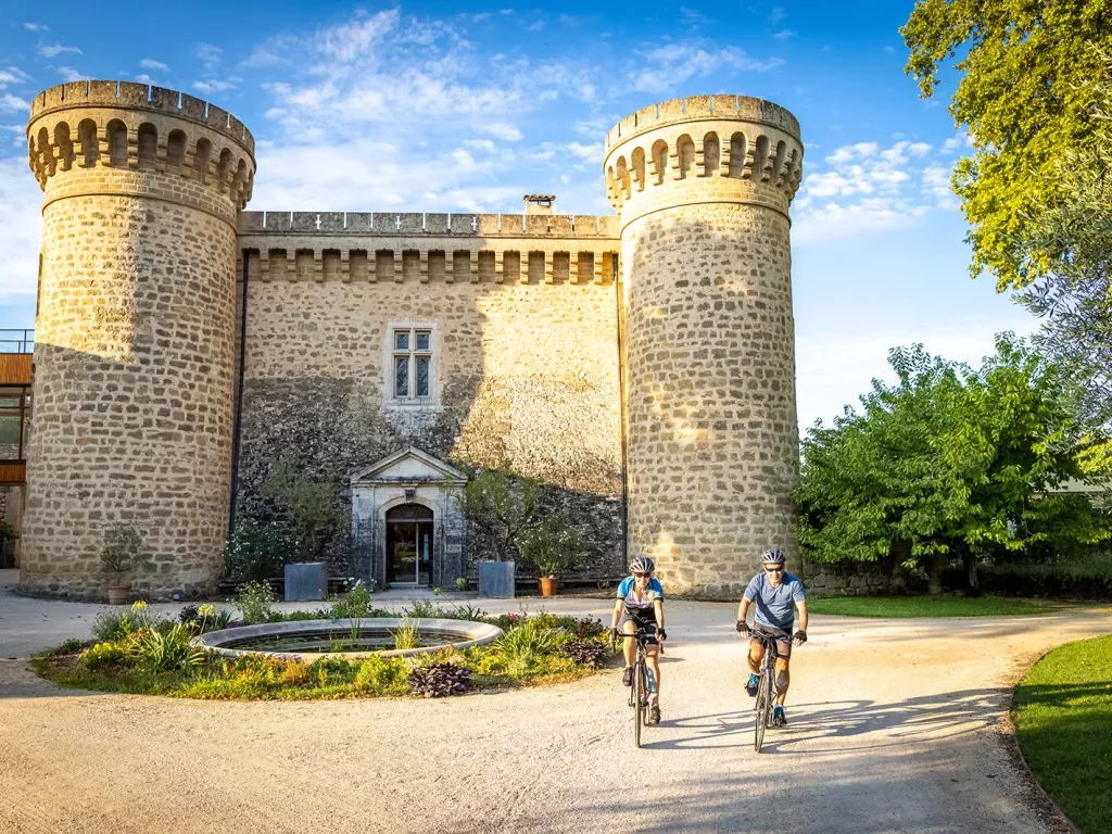 Two guests cycling in front of large stone brick castle.