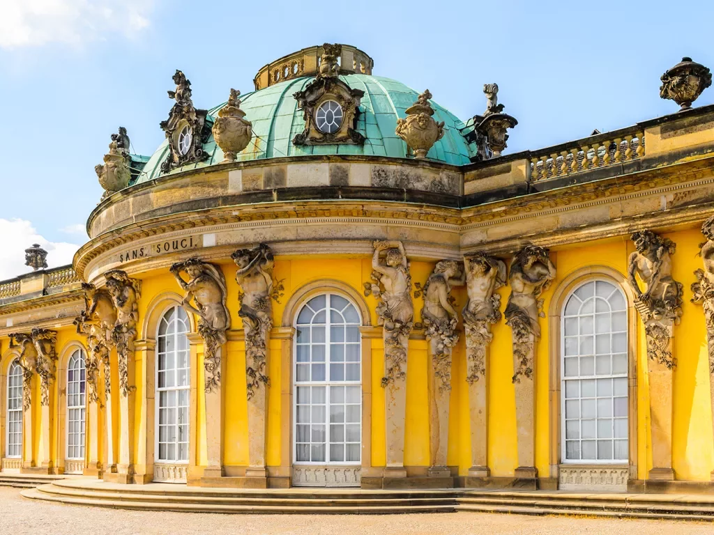 Sans Souci building in Germany, bright yellow decorated with statues of cherubs.