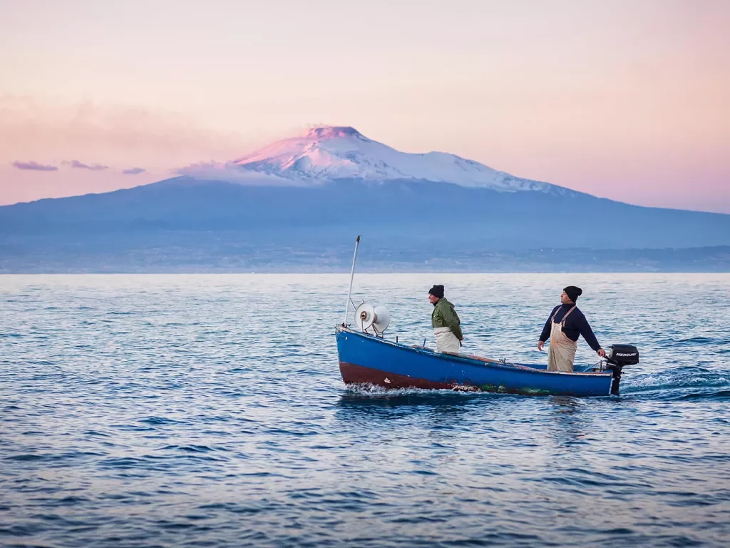 Two locals on boat during sunset, large mountain in distance.