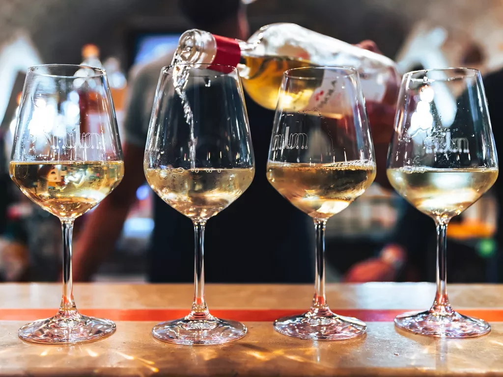 Server pouring white wine into four glasses.
