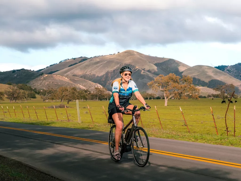 Guest cycling down California farm road, cows and hills in background.