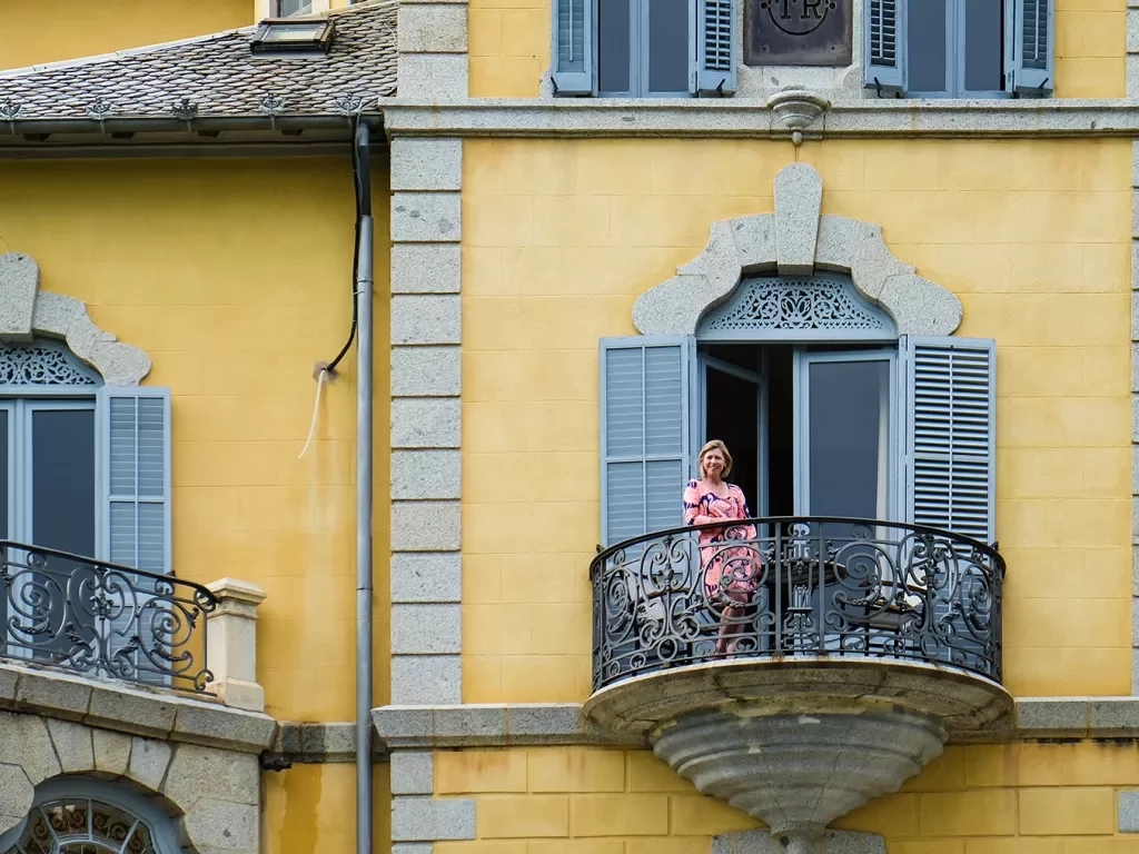Woman standing on balcony of yellow building. 