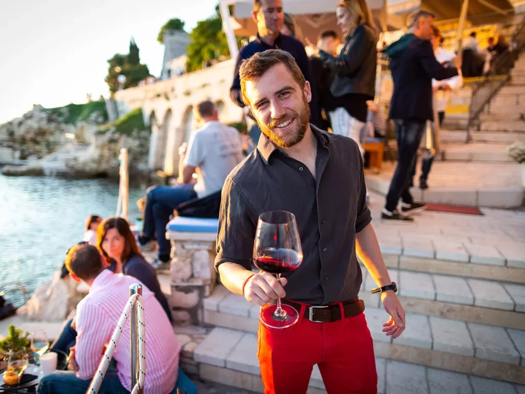 Man among group of other people, wine glass in hand, sunset.