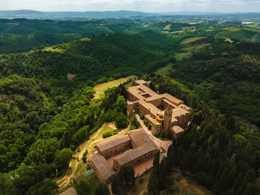 Bird's eye shot of Italian countryside, forests, castle, hills visible.