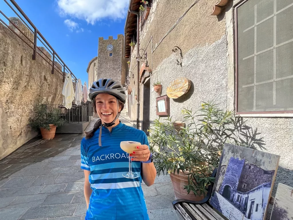 Guest in bike clothes holding cocktail, tan-stone walls surround them.