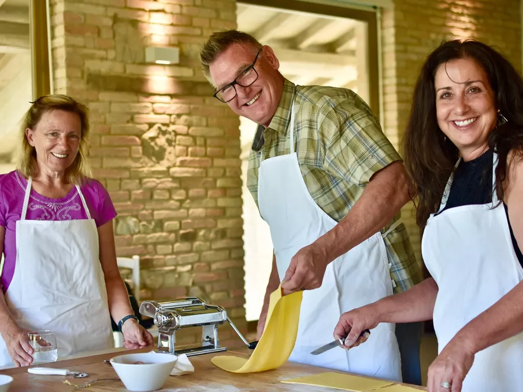 People smiling at the camera while rolling out pasta dough
