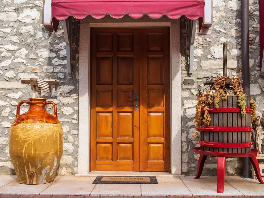 Stone storefront, large ceramic vase, wine grape crusher, wood door.