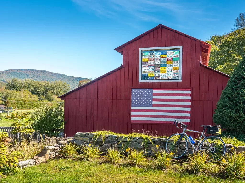 Shot of bike in front of red barn, US flag on barn wall.