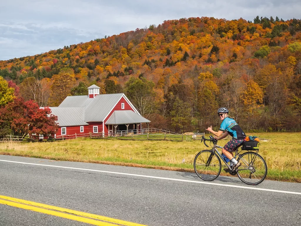 Guest cycling past red farmhouse. Fall trees behind.