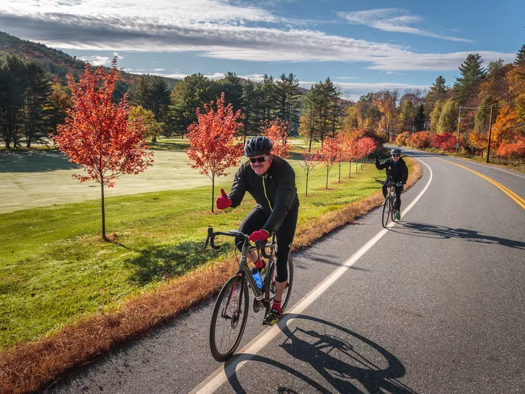 Two guests cycling down autumnal road, both giving thumbs-ups.