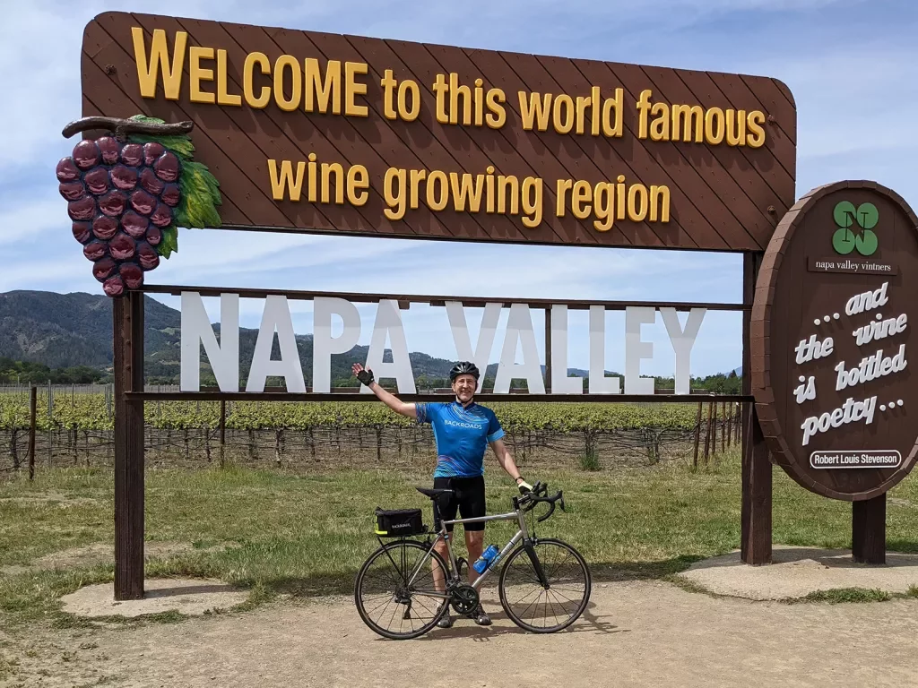 Guest with bike in front of "WELCOME TO NAPA VALLEY" sign.