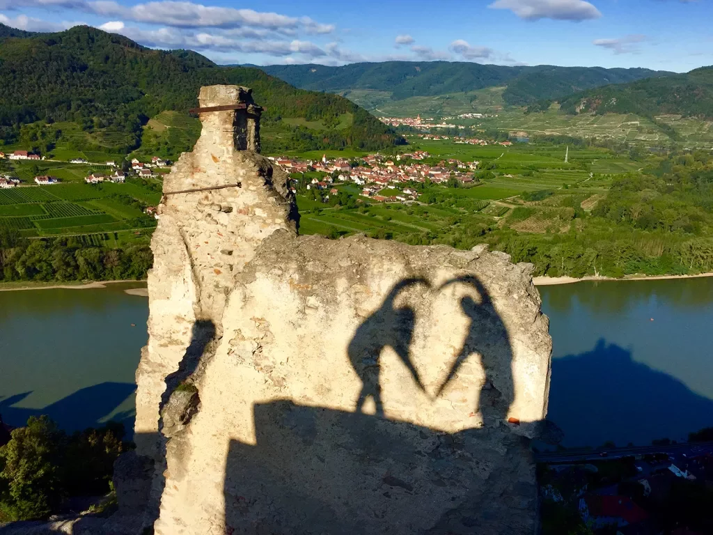 Shadows of two people making a heart with their arms.