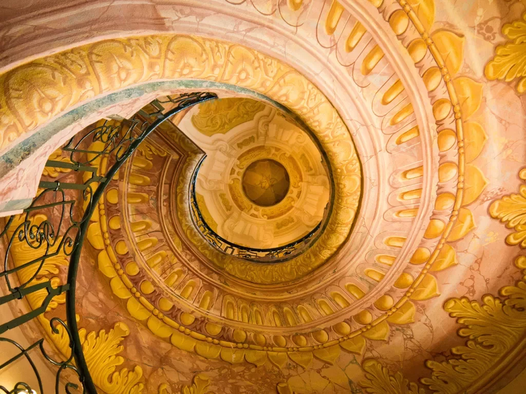 Ornate yellow and golden painted staircase spiraling to the ceiling.