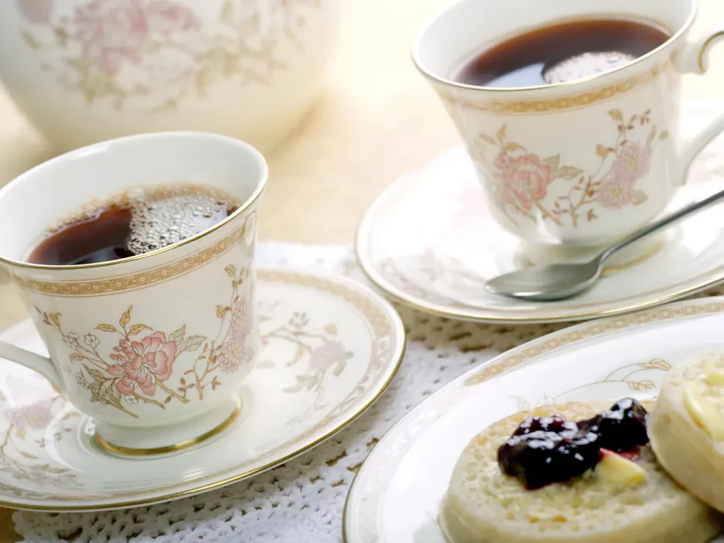 Ornate English cups of tea and english muffins with butter and jam.