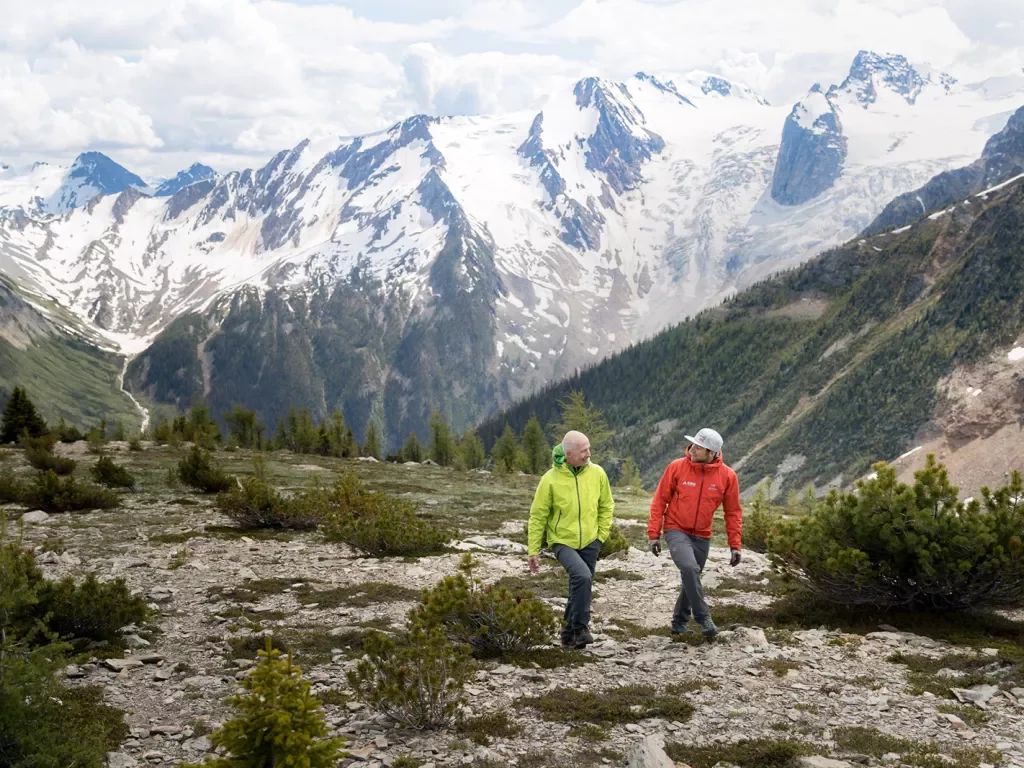 Two guests walking on hillside, Bugaboos in background.