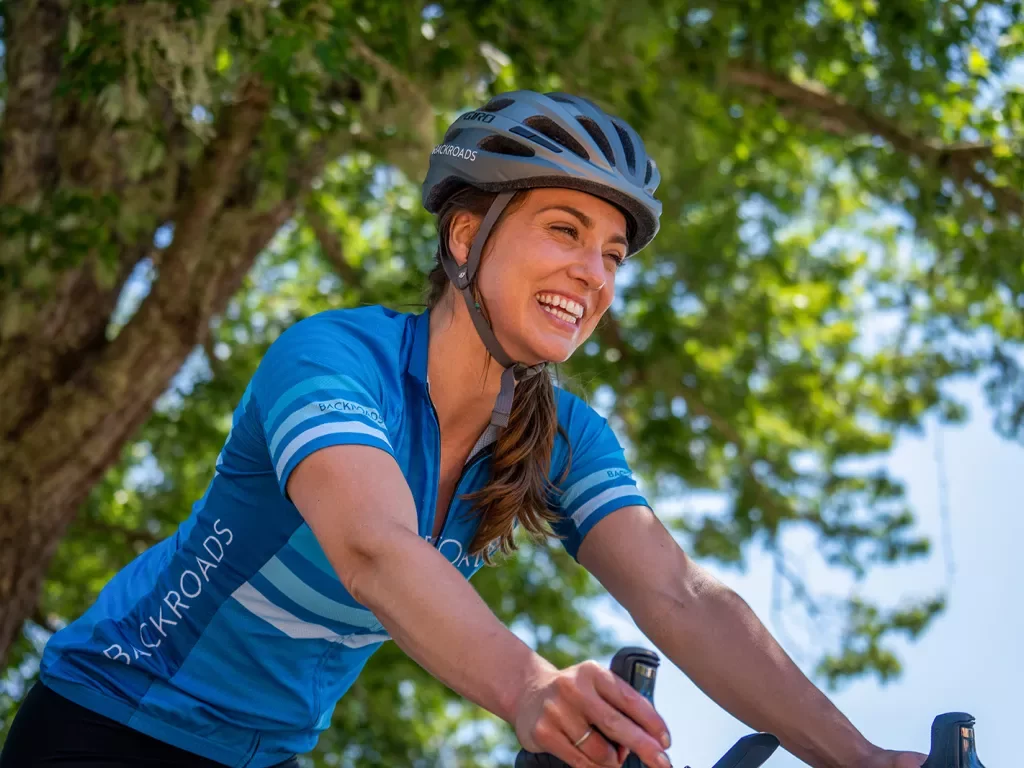 Guest on bike with gear smiling, tree above her.