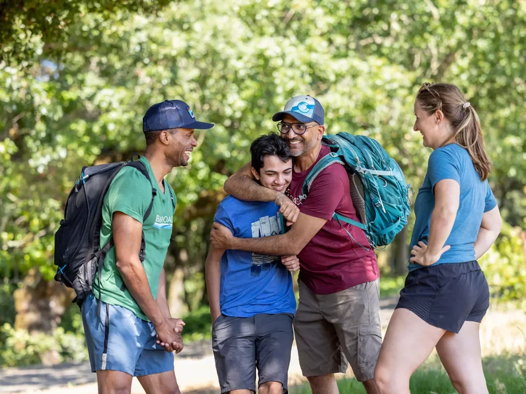 Four guests on the trail, smiling at each other, one is hugging another.