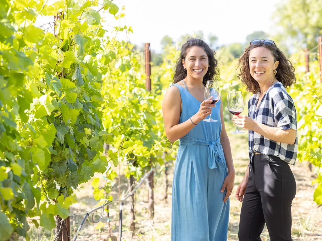 Two guests among the grapevines, wine glasses in hand.