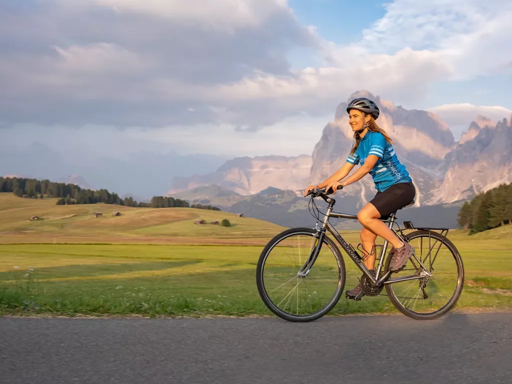Guest cycling on road, meadow and large mountain in background.