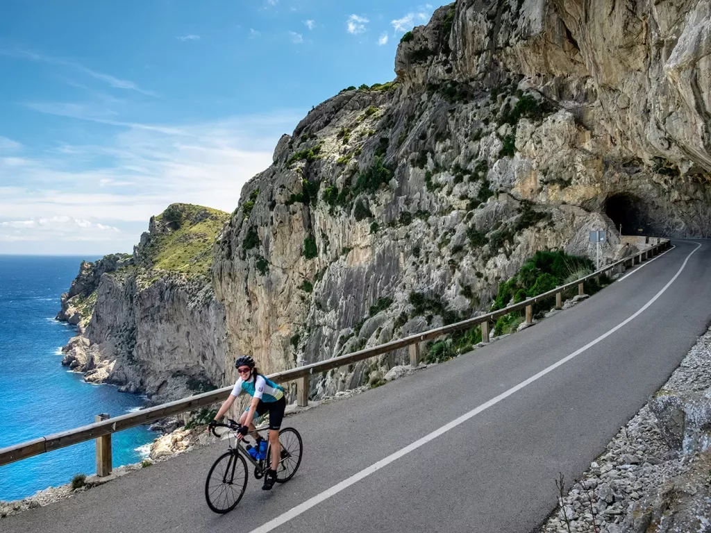 Guest cycling down coastal cliffside road, road coming from cave, ocean to  her right.