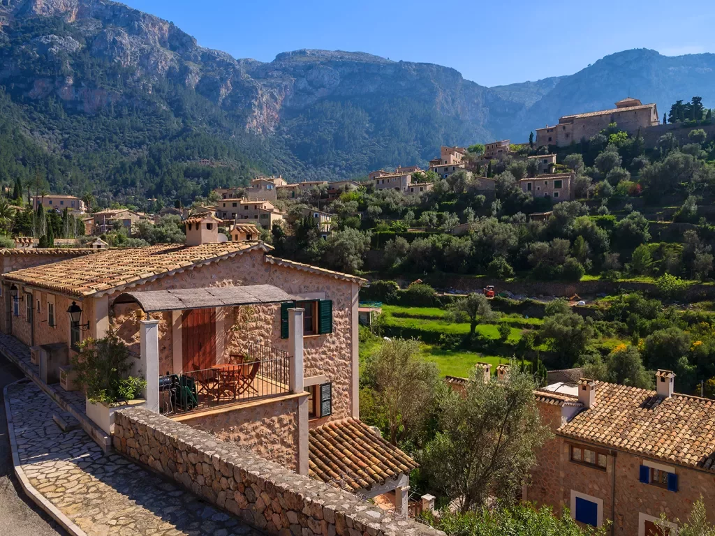 Shot of Italian mountain village, tan stone houses, trees, mountains all around.