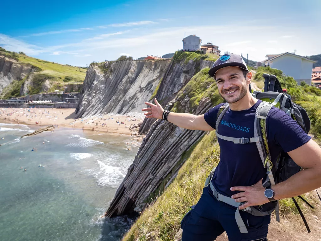Leader gesturing to craggy cliffs, large beach, buildings dotting cliffside.