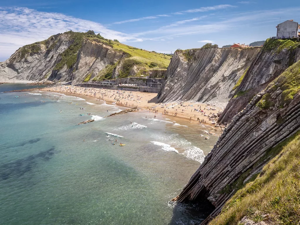 Shot of craggy cliffs, large, crowded beach in distance. 
