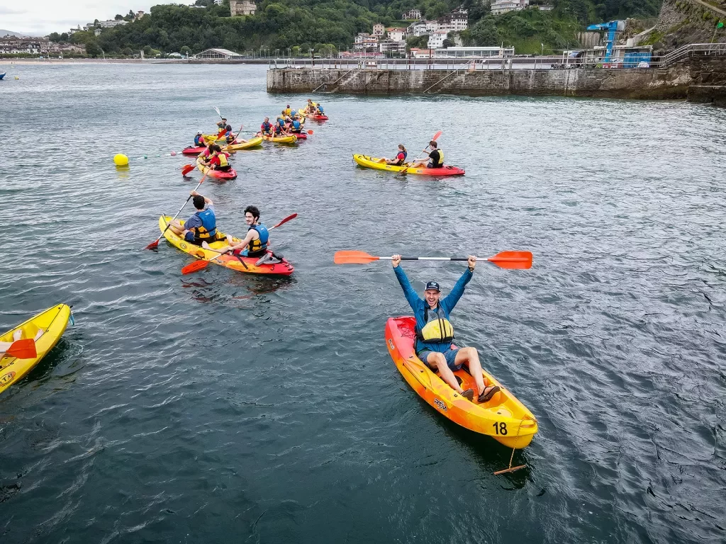 Group of guests in kayaks, one raising paddle over head, coast behind them.