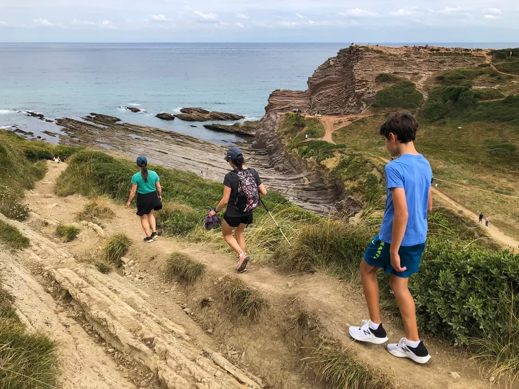 Three guests walking towards coastline, craggy cliffs.