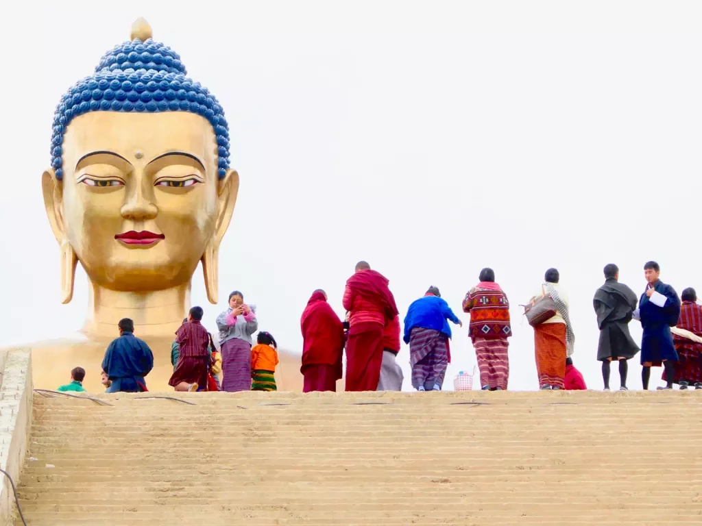 Group of travelers at the top of a large staircase standing before a large, gold Buddha head