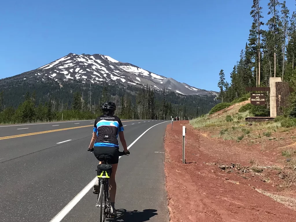 Guest cycling past "MT. BACHELOR" sign, the mountain itself in the background.