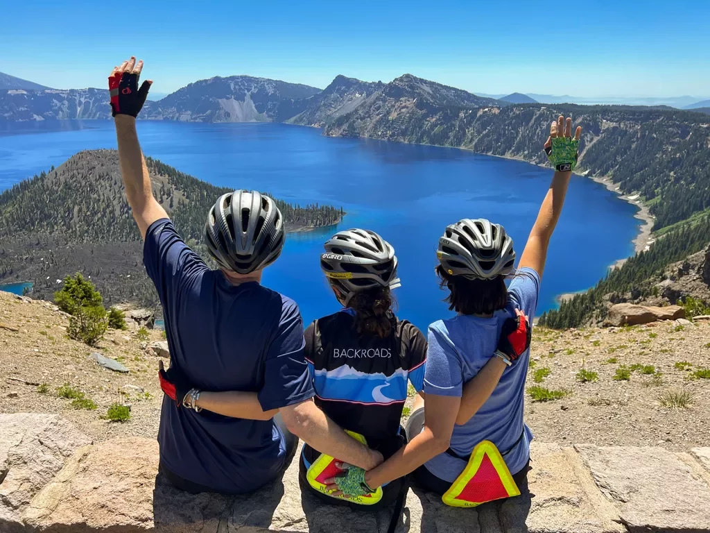 Three guests with their hands above their heads, celebrating on he rim of Crater Lake.