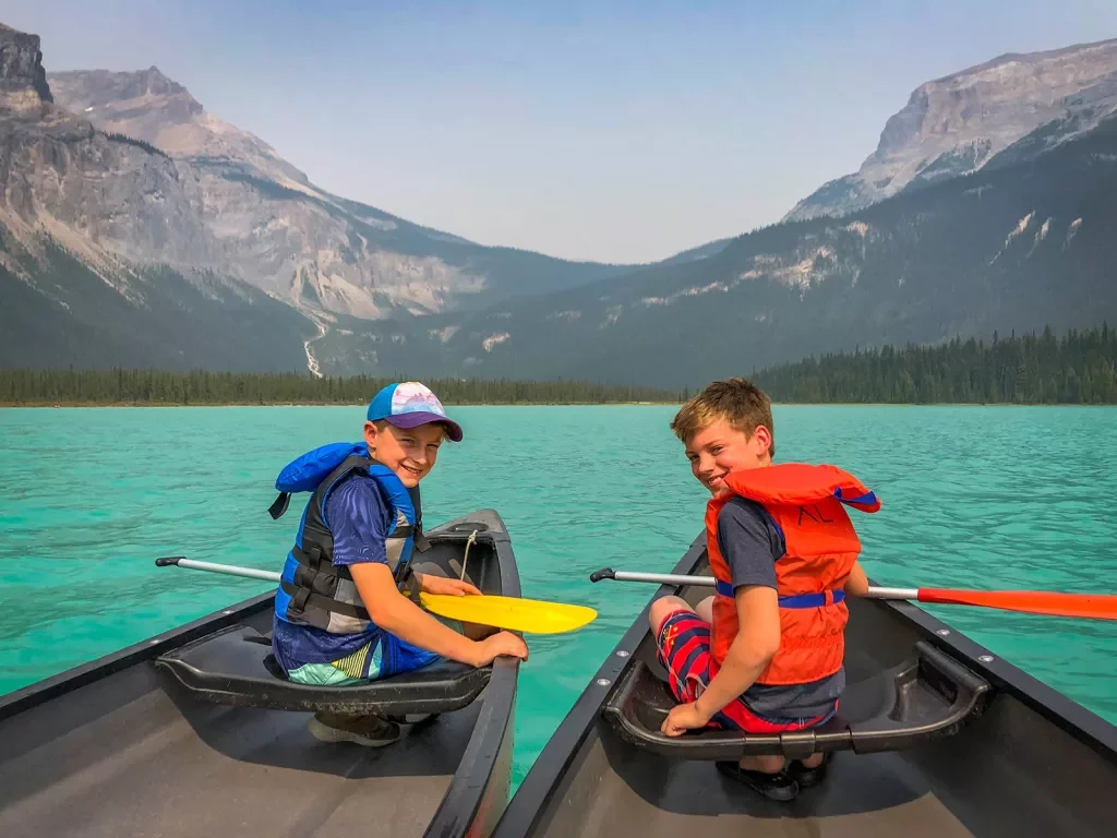 Two young guests in canoes, Rockies in distance.