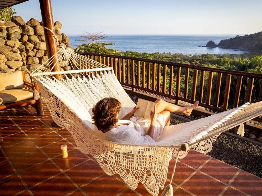 Guest on hotel balcony, hammock, overlooking forest, ocean.