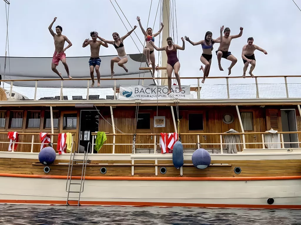 Group of guests jumping off large wood panel boat.