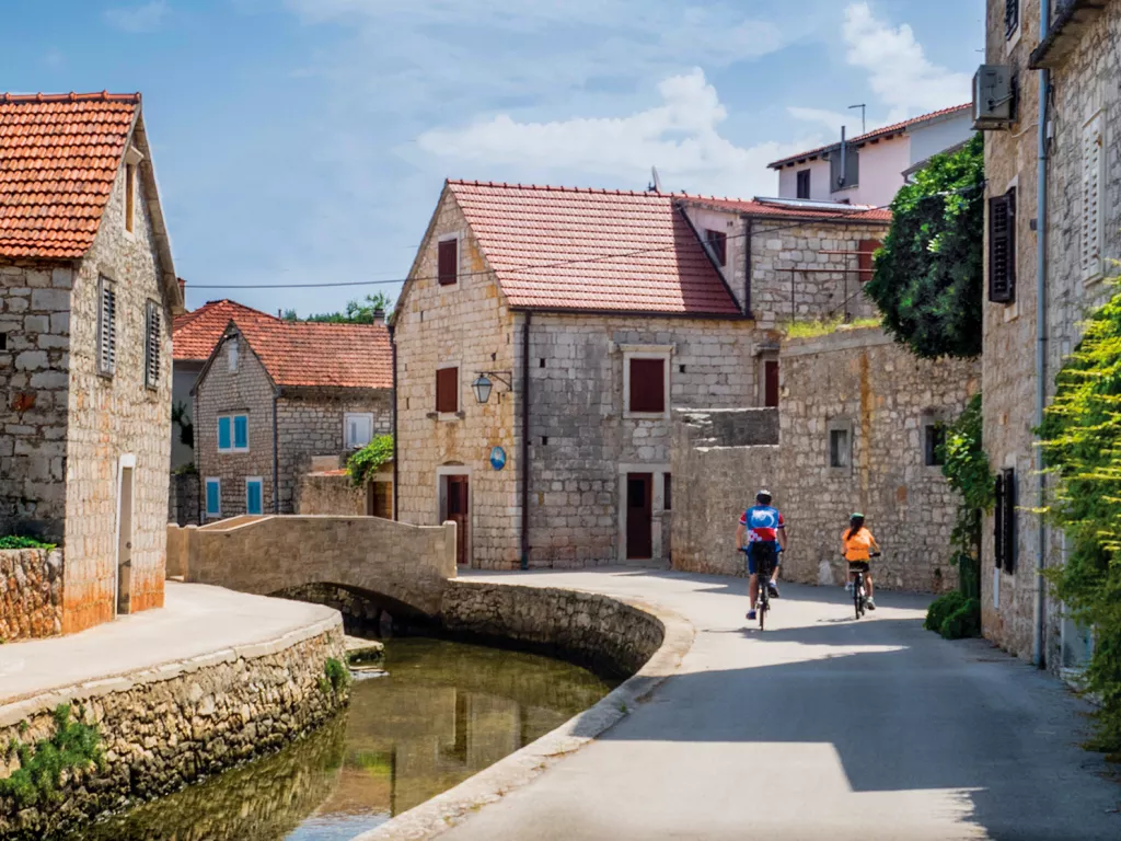 Two guests biking through old style town, river beside them.