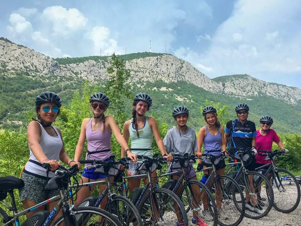 Group of guests with bikes, posing for camera, large mountain behind them.