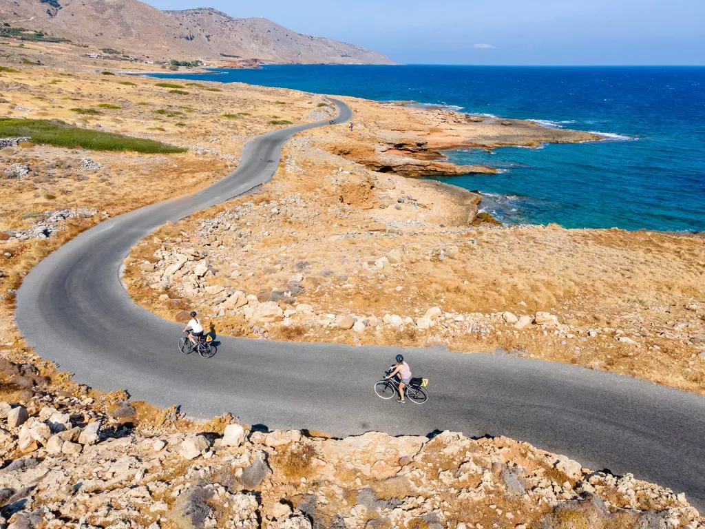 Two guests cycling along golden coastline, ocean to their right.