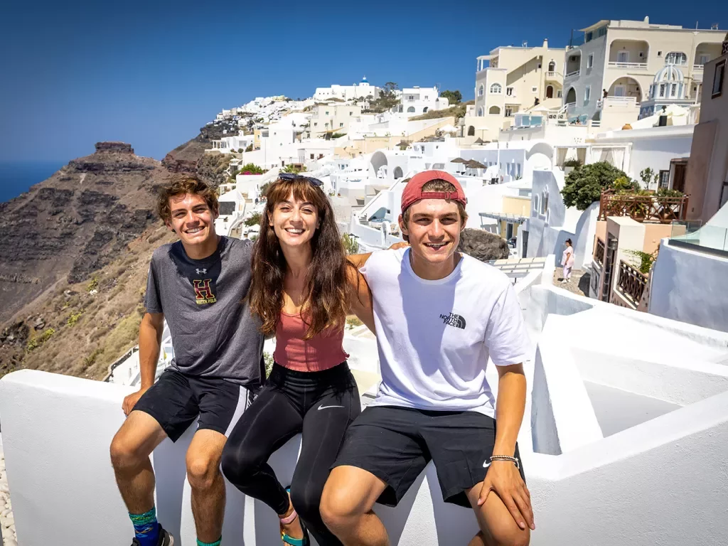Three young guests sitting on ledge overlooking cliff, white hillside houses behind them.