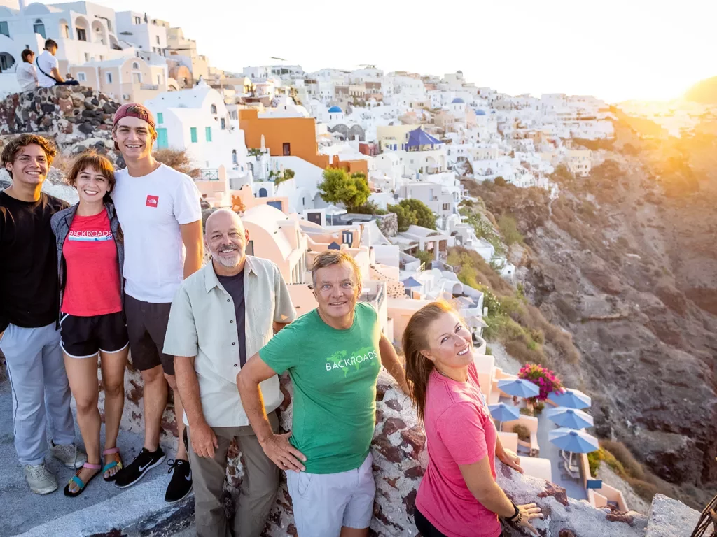 Group of guests among cliffside, whit houses, sunset behind them.