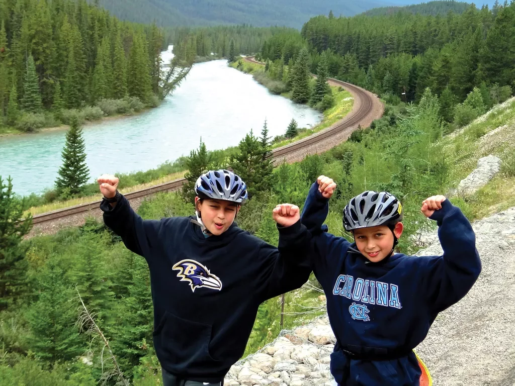 Two young guests with their hands above their heads, river, forest, road behind them.