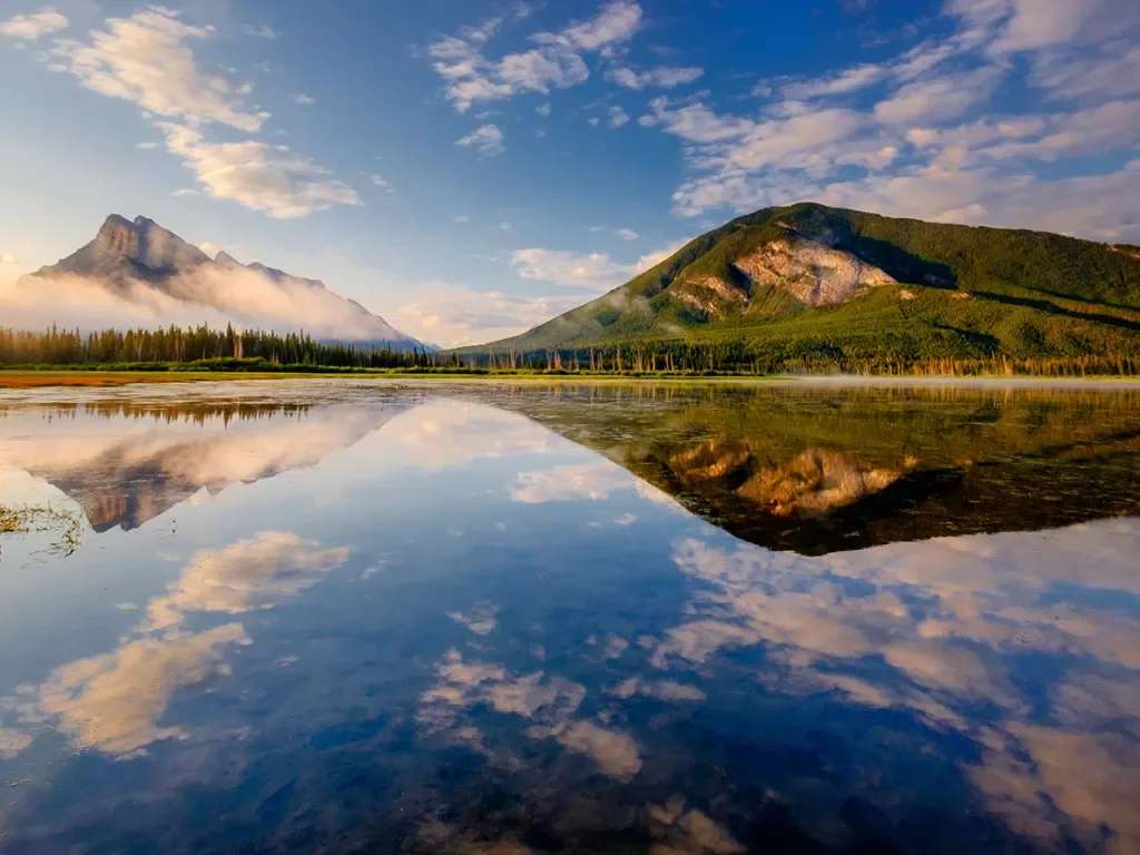 Wide shot of reflective lake, mountains during sunset.