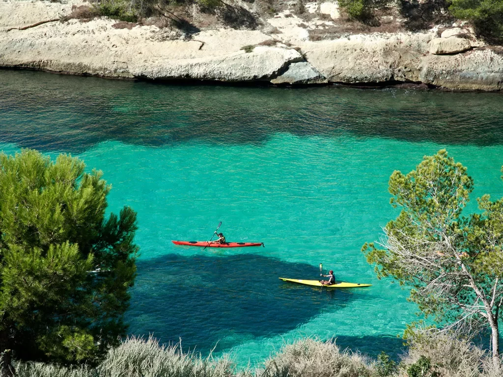 Wide shot of two guests kayaking through blue water.