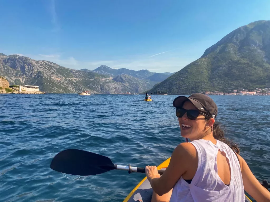 Guest kayaking, looking at camera. Large mountains behind her.