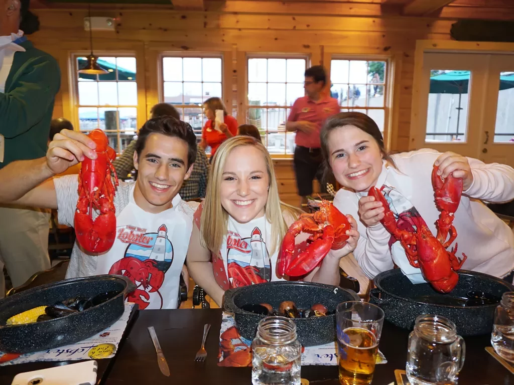 Three young guests holding up cooked lobsters during a meal.