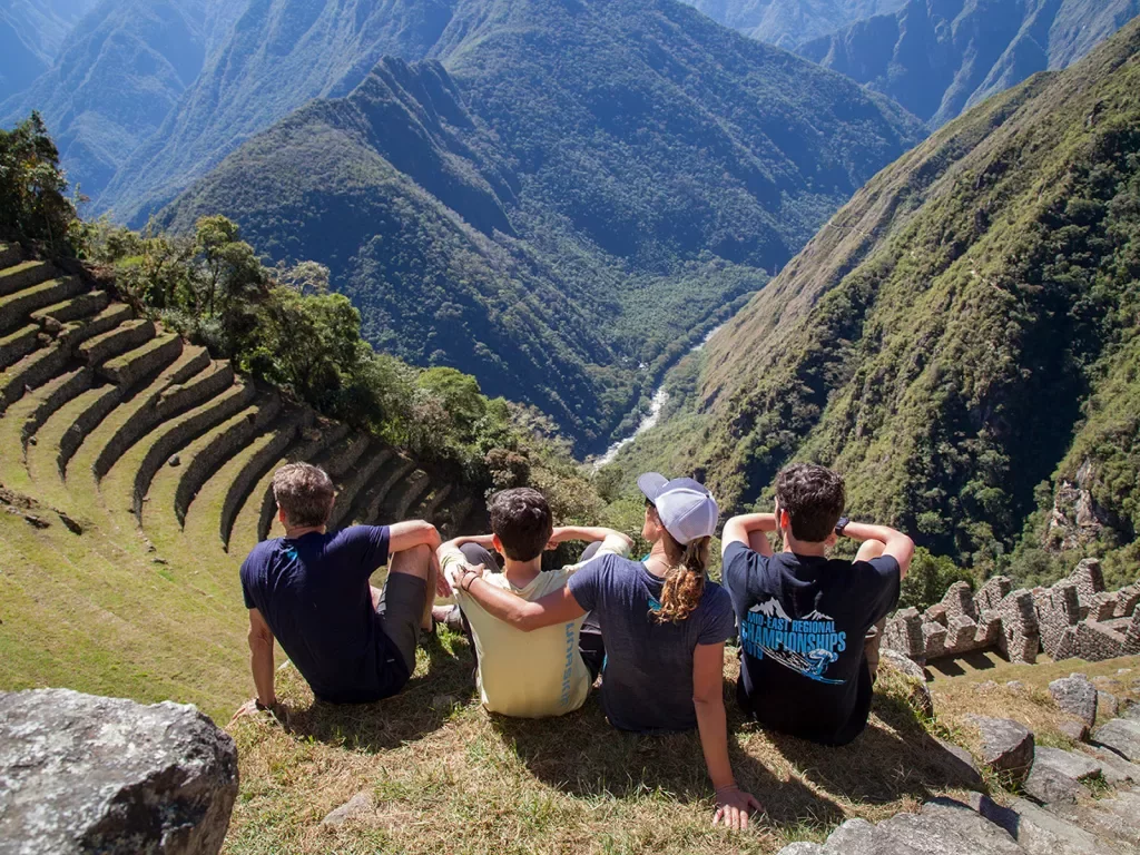 Four guests sitting on Machu Picchu hillside, overlooking mountains. 