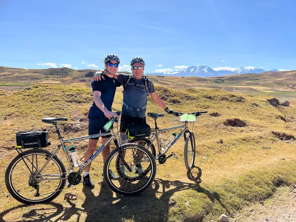 Two guests with bikes on golden meadow, mountains behind them.