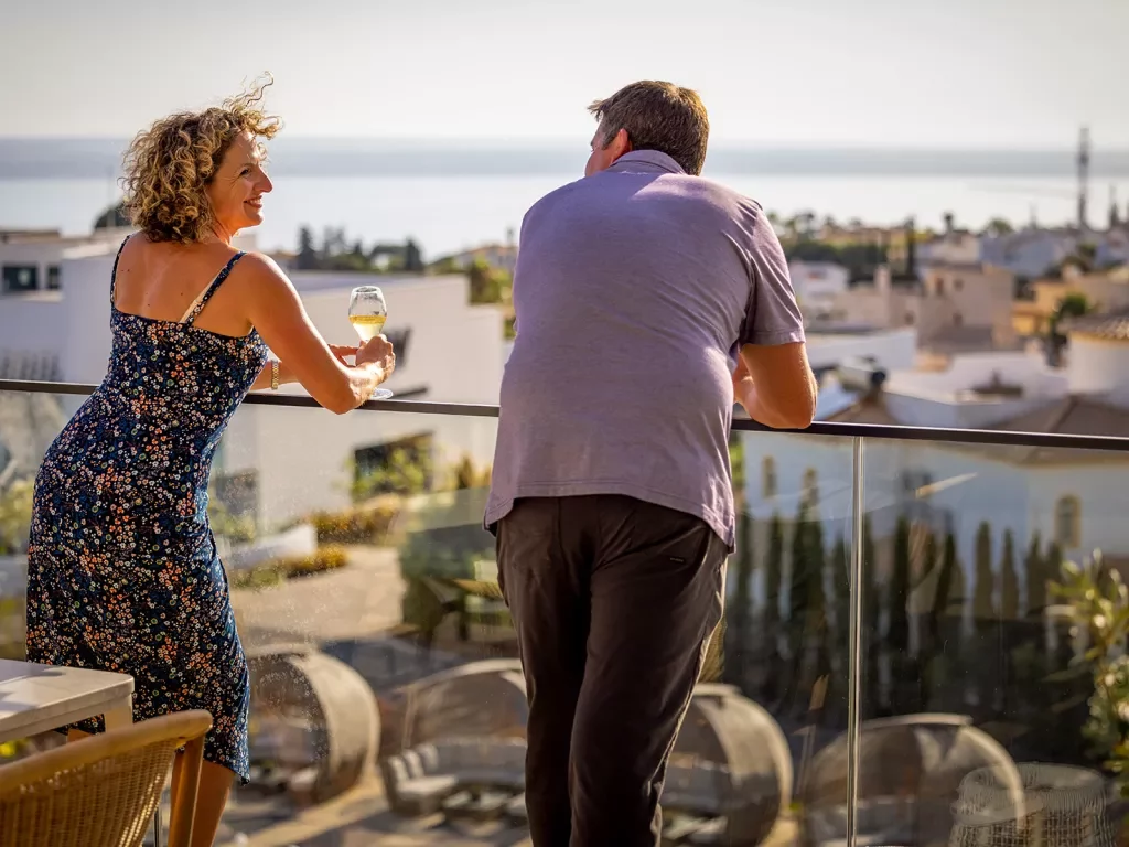 Two guests standing on a balcony overlooking a town on the sea