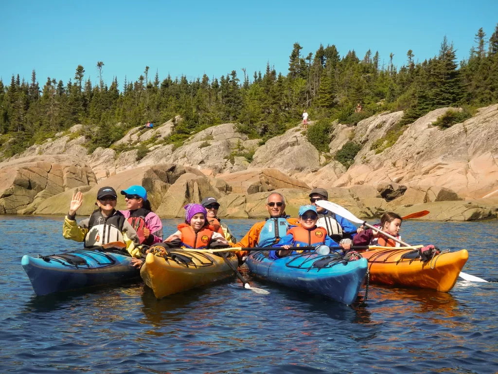 Group of kayaking guests, rocky shore and forest in background.