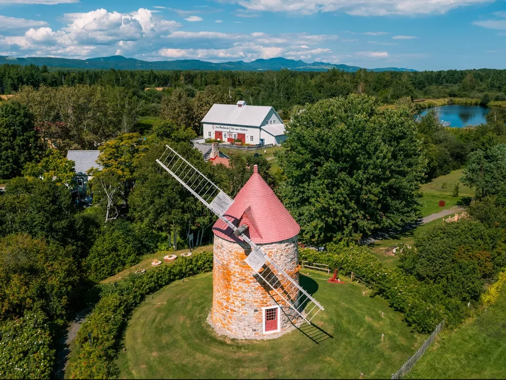 Wide shot of large windmill, white building in background.